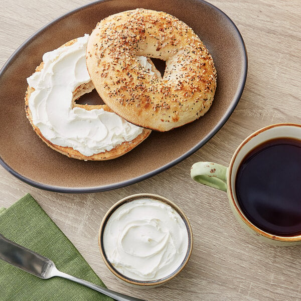 A bagel with Philadelphia Reduced Fat Cream Cheese and seeds on a plate with a cup of coffee on a table.