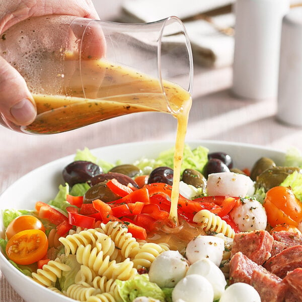 A person pouring Regal Italian dressing onto a salad with pasta, meat, and vegetables.