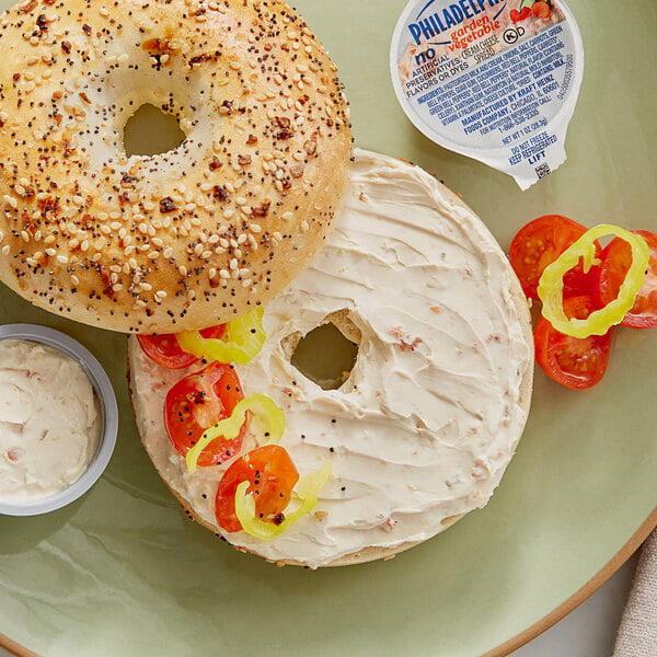 A bagel with Philadelphia Garden Vegetable Cream Cheese spread and tomatoes on a plate.