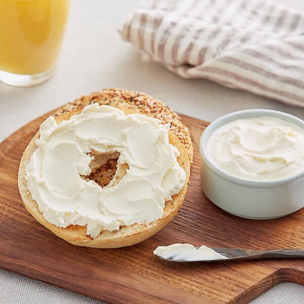 A bagel with Philadelphia Cream Cheese on a wooden board.