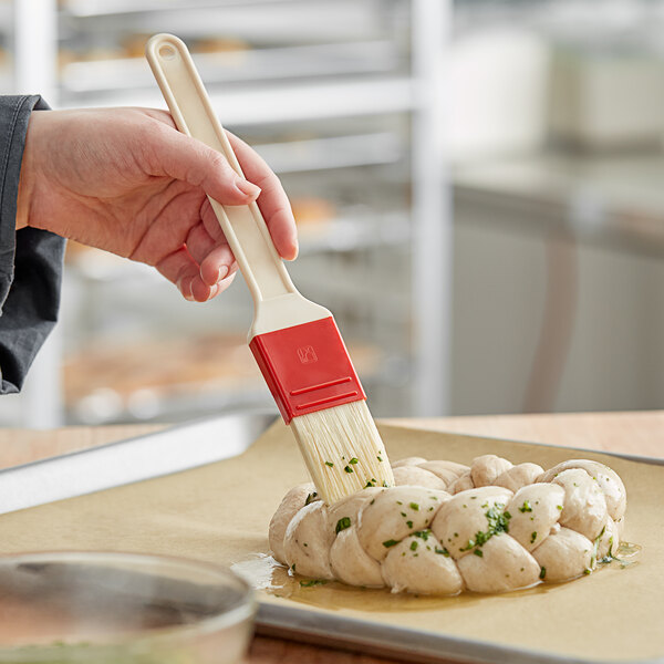 A hand using a Choice natural bristle pastry/basting brush to brush food.