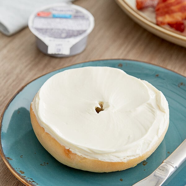 A blue plate with a bagel with Philadelphia reduced fat cream cheese spread.