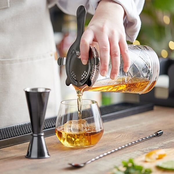 A hand using an Acopa cocktail spoon to stir a drink in a glass.