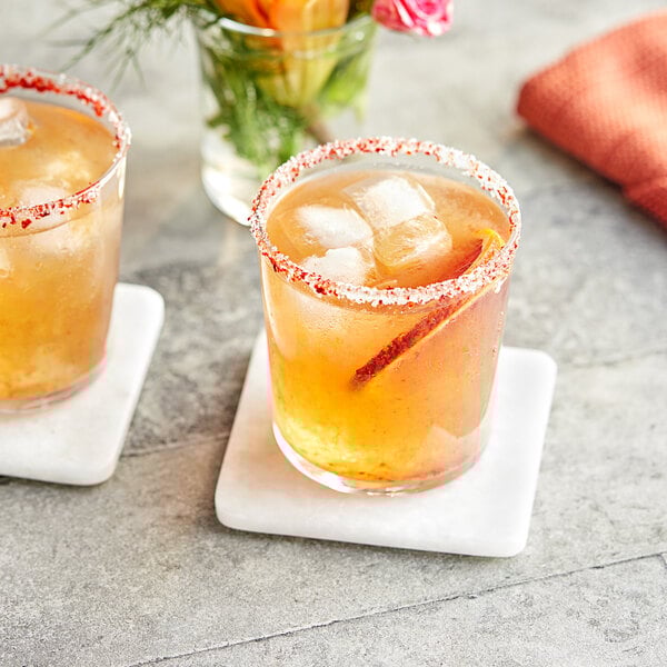 A glass with ice and orange liquid next to a drink with ice and a flower.