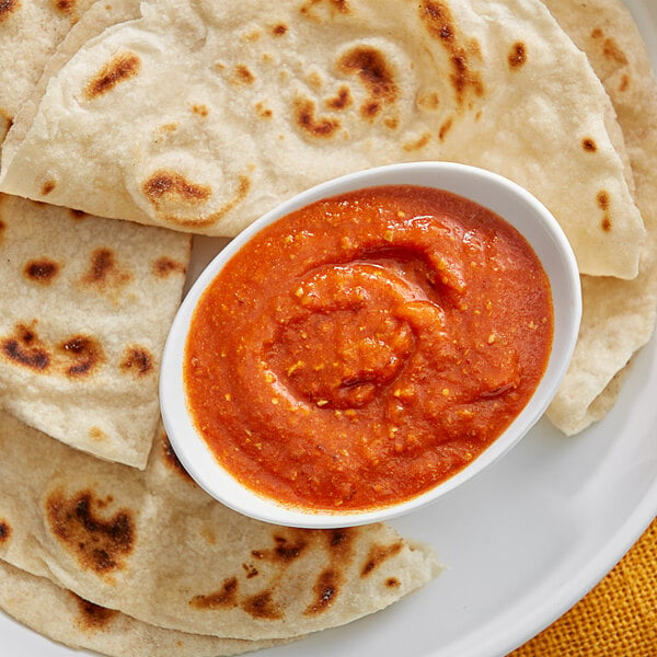 A plate of tortillas with a bowl of Ashoka Chatpata Achari red sauce.