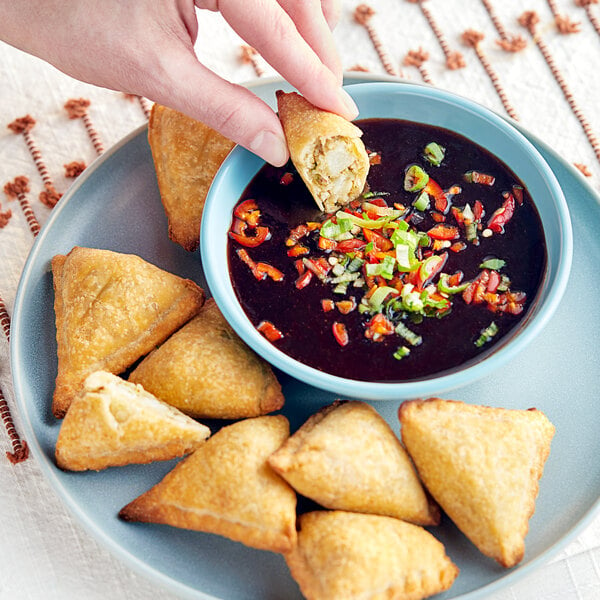 A hand holding a piece of food dipping into a bowl of Ashoka Date and Tamarind Chutney.