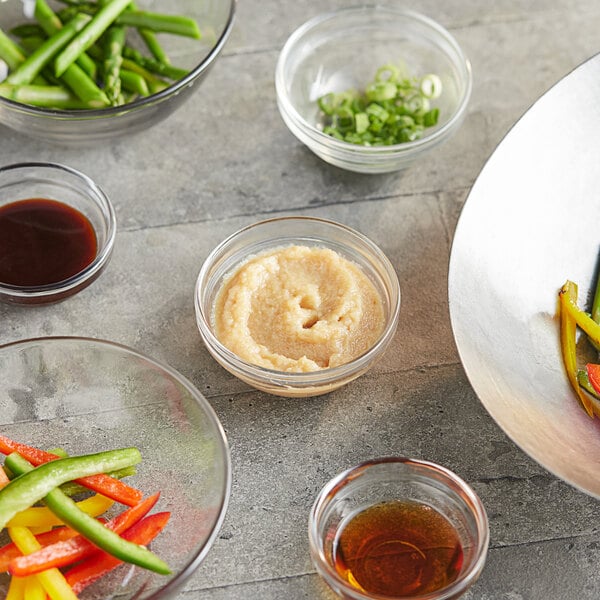 A table with bowls of Ashoka Garlic Paste and chopped green onions alongside a bowl of vegetables.