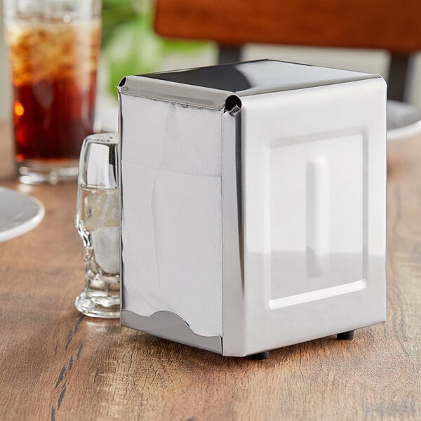 A stainless steel low-fold napkin dispenser on a table in a pizza parlor.