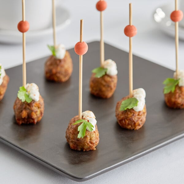 A plate of meatballs on Front of the House orange bamboo ball picks with cheese and greens.