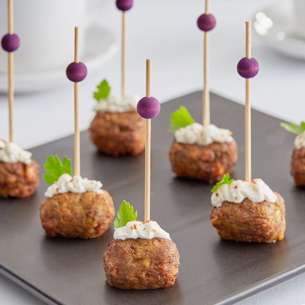 A plate of meatballs with purple bamboo ball picks and green leaves.