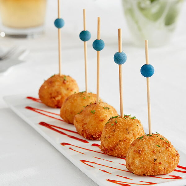 A plate of food with Front of the House Blue Bamboo Ball Picks on a table.