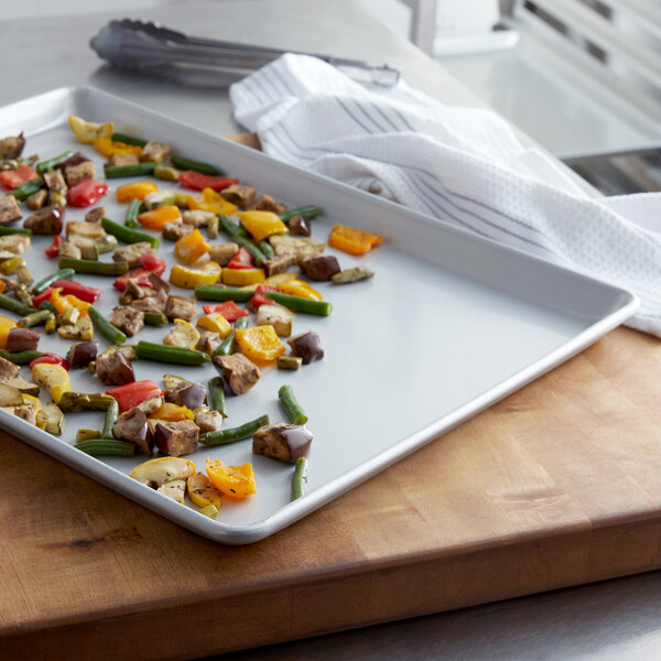 A Chicago Metallic wire in rim bun pan holding vegetables on a wooden surface.