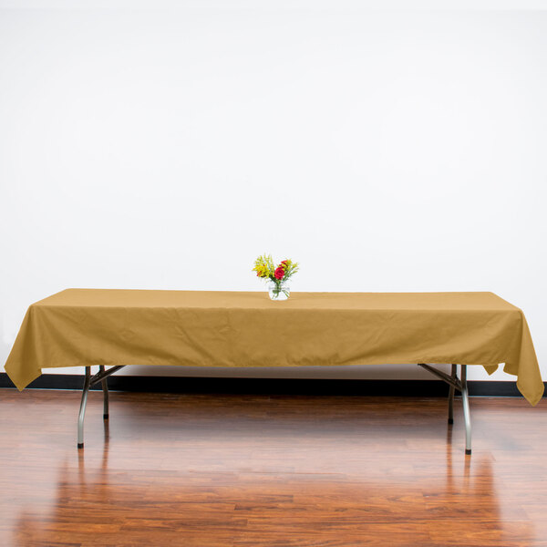 A table with a yellow Intedge tablecloth on it with a glass vase of flowers.
