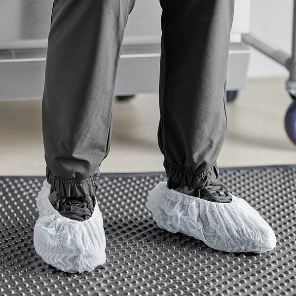 A person wearing Choice white polypropylene shoe covers over shoes with a skid-resistant bottom.