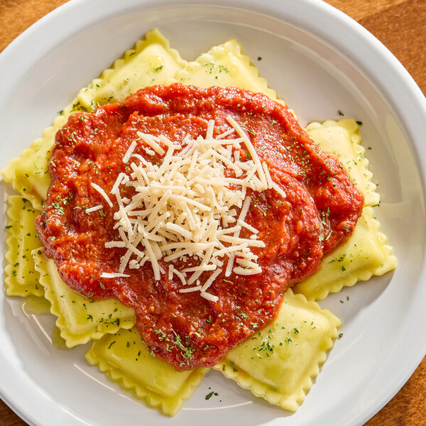 A plate of ravioli topped with tomato sauce and a generous amount of shredded vegan parmesan cheese.