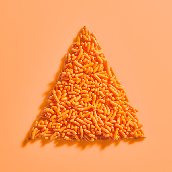 A pile of orange sprinkles arranged in a triangle shape on an orange background.