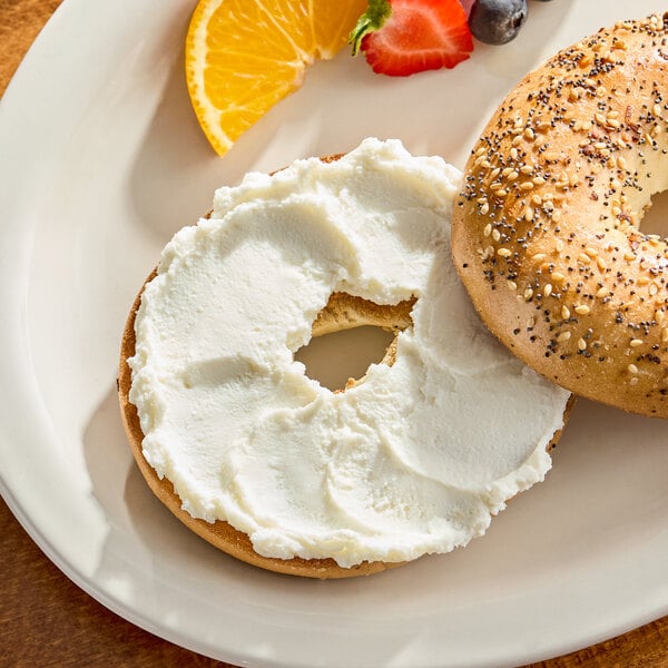 A bagel with dairy-free vegan cream cheese served on a plate with fruit slices.