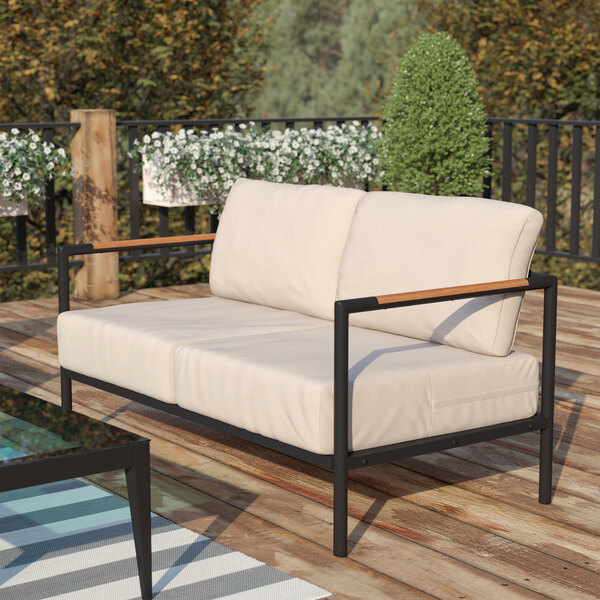 A Flash Furniture teak loveseat with white cushions on a wood deck.