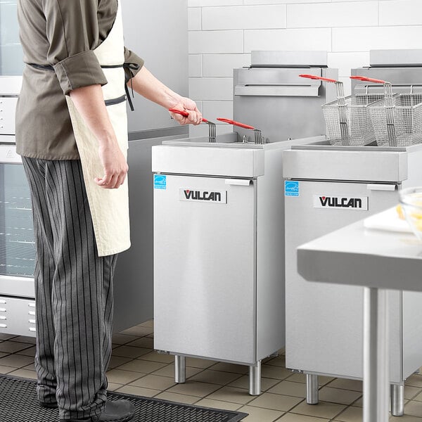 A man in a white apron using a Vulcan natural gas fryer in a professional kitchen.