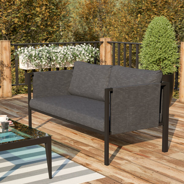 A Flash Furniture charcoal loveseat with storage pockets and a glass table on a deck.