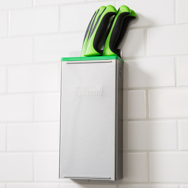 An Edlund stainless steel knife rack with a green and black insert on a wall.