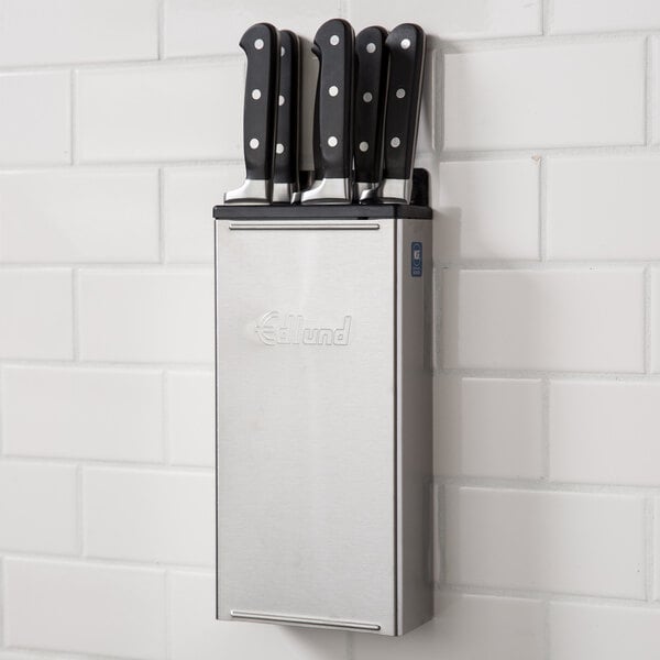 An Edlund stainless steel knife rack on a white wall with knives in it.