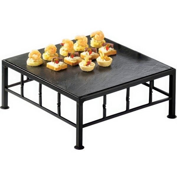 A Cal-Mil black metal square riser with food on it.