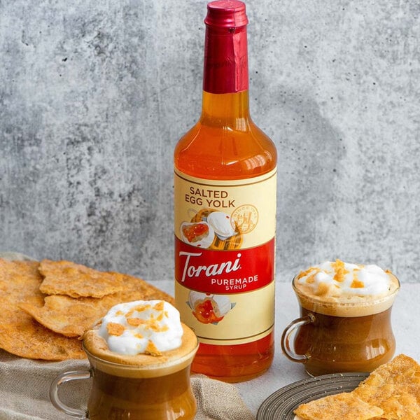 A bottle of Torani Puremade Salted Egg Yolk flavoring syrup next to a glass of a drink.