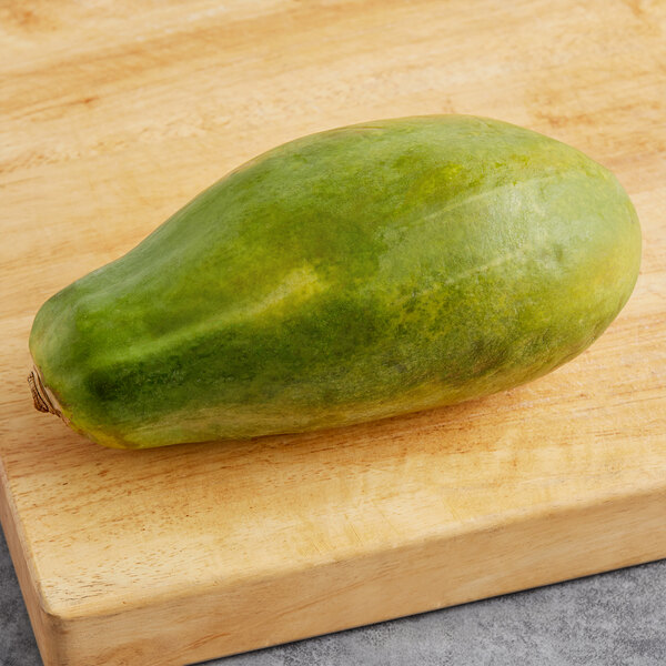 A green Tainung-Type papaya on a wooden cutting board.