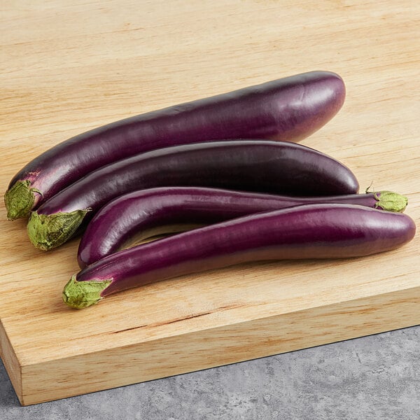 Three fresh Chinese eggplants on a wooden cutting board.