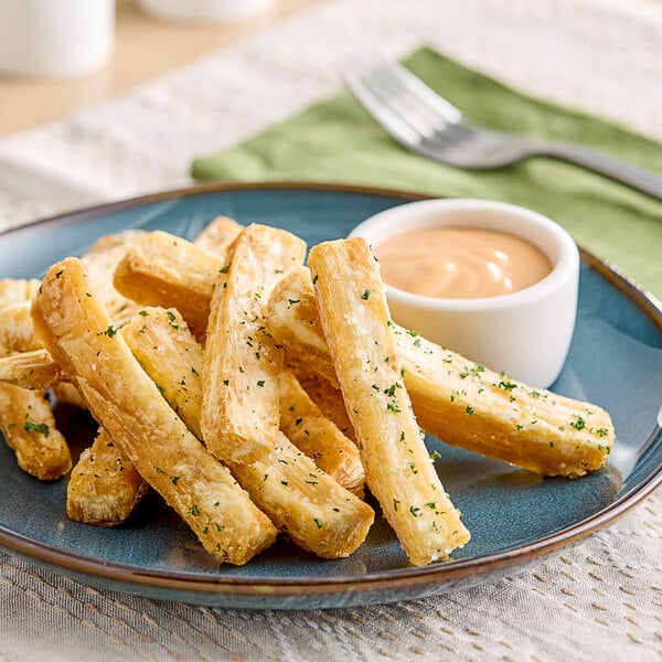 A plate of fresh yuca fries with sauce on a white surface.