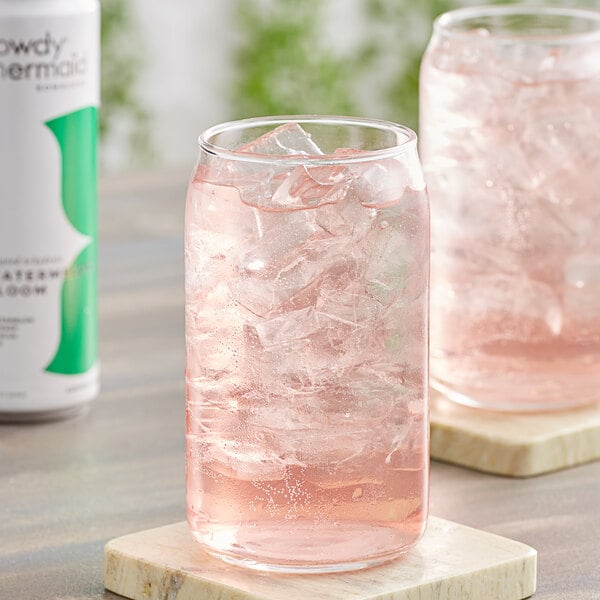 A glass of Rowdy Mermaid Watermelon Bloom Kombucha with ice on a wooden tray.