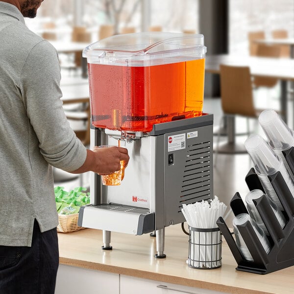 A person pouring a drink into a Crathco refrigerated beverage dispenser.