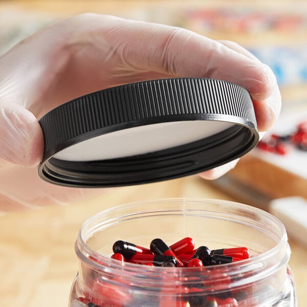 A hand using a black child-resistant cap to close a container of pills.