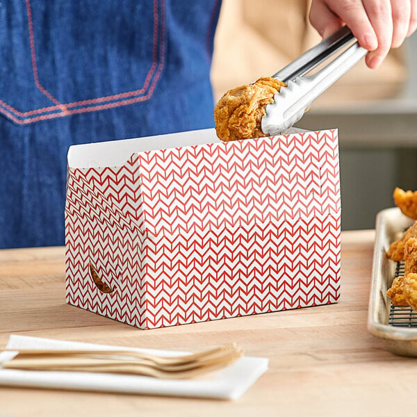 A person holding a red and white Choice Cornerstone Take-Out box with fried chicken inside.