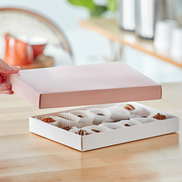 A hand holding a pink linen candy box with a black border.