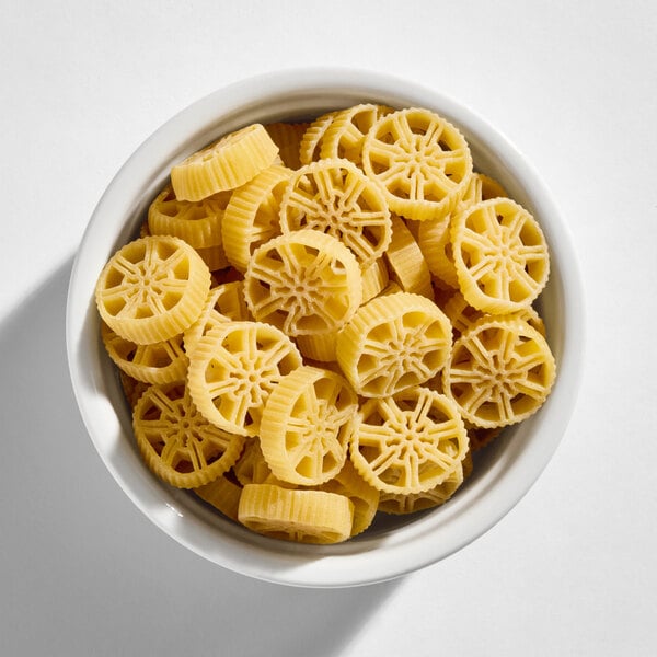 A white bowl filled with uncooked, wheel-shaped pasta pieces.