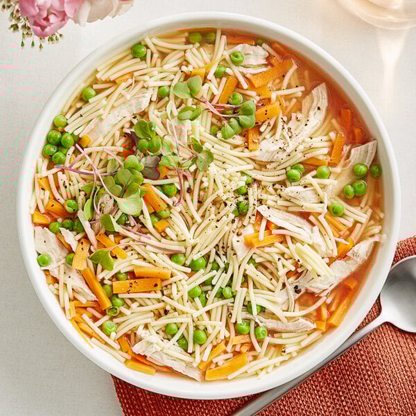 A bowl of chicken noodle soup with Barilla Fideo Pasta, carrots, and peas.