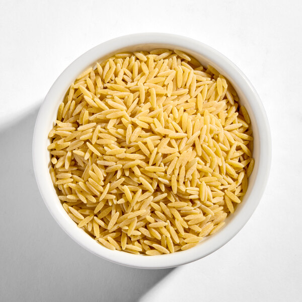 A white bowl filled with uncooked orzo pasta.