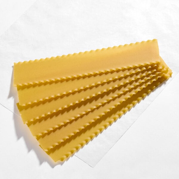 A set of uncooked wavy lasagna noodles arranged in a fan shape on a white surface.