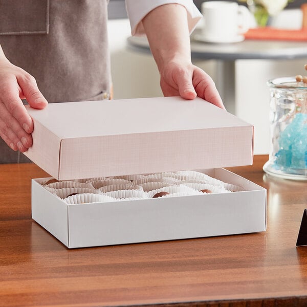 A person holding a white rectangular 9 3/8" x 6" x 2" pink linen candy box.