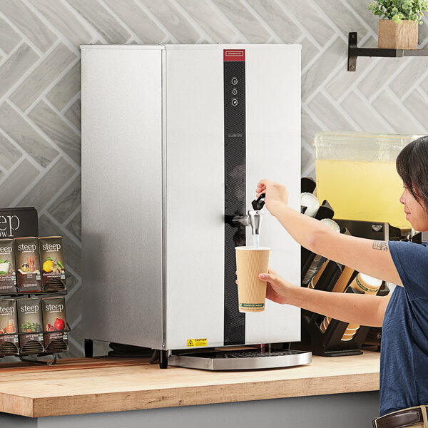 A woman using a Grindmaster tap-operated hot water dispenser to fill a cup.