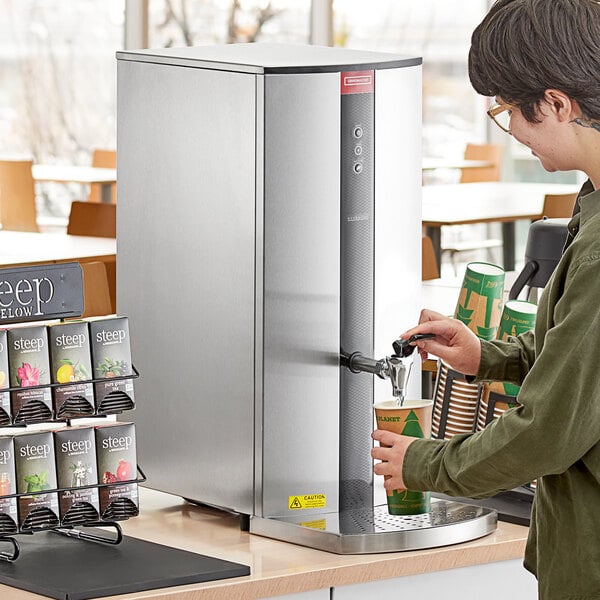 A man using a Grindmaster tap-operated hot water dispenser to fill a cup.