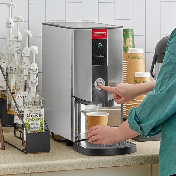 A woman using a Grindmaster hot water dispenser to fill a cup.