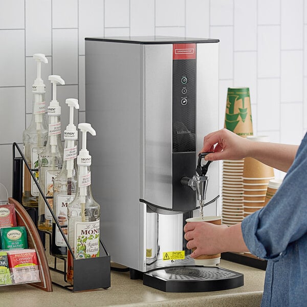 A person using a Grindmaster hot water dispenser to fill a coffee machine with water.