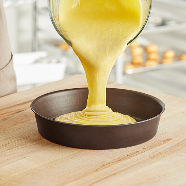Batter being poured from a bowl into a Gobel round non-stick cake pan.