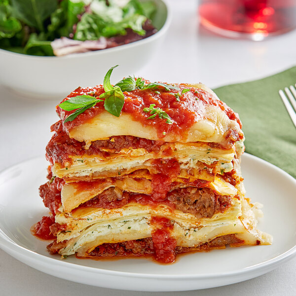 A plate of Barilla oven ready lasagna with a fork and a bowl of salad.