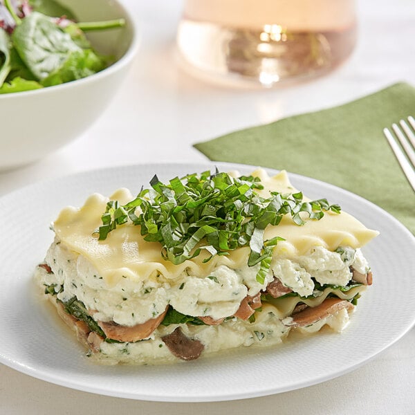 A white plate topped with a layer of Barilla Wavy Lasagna and a salad.