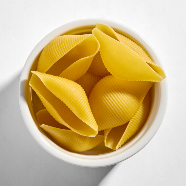 A white bowl filled with uncooked Barilla jumbo shell pasta.