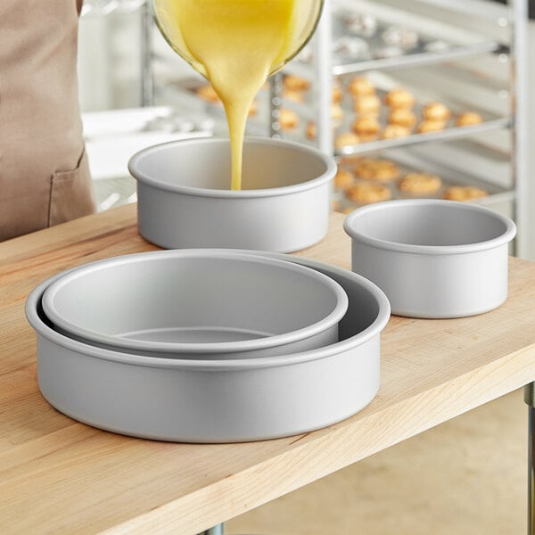 A person pouring yellow liquid into a round cake pan.